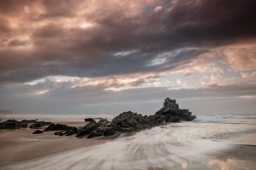 body of water near rock formation with nimbus cloud