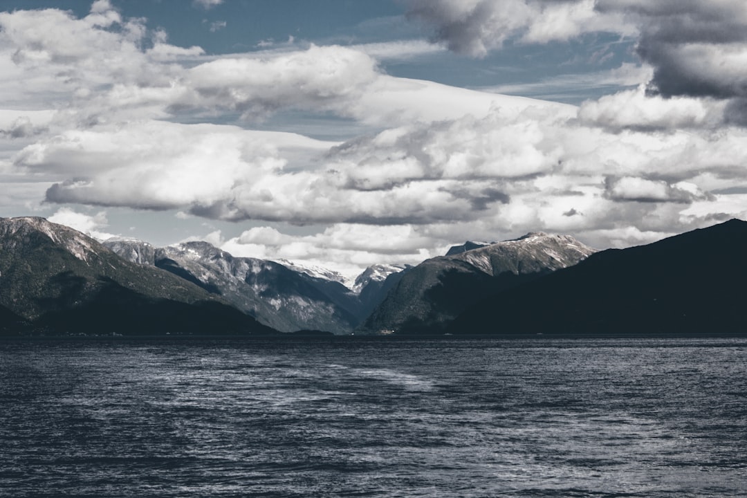 mountain near body of water under white skies at daytime,