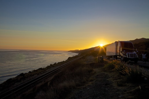 A fleet of trucks loaded with cargo driving along a coastal highway at sunset