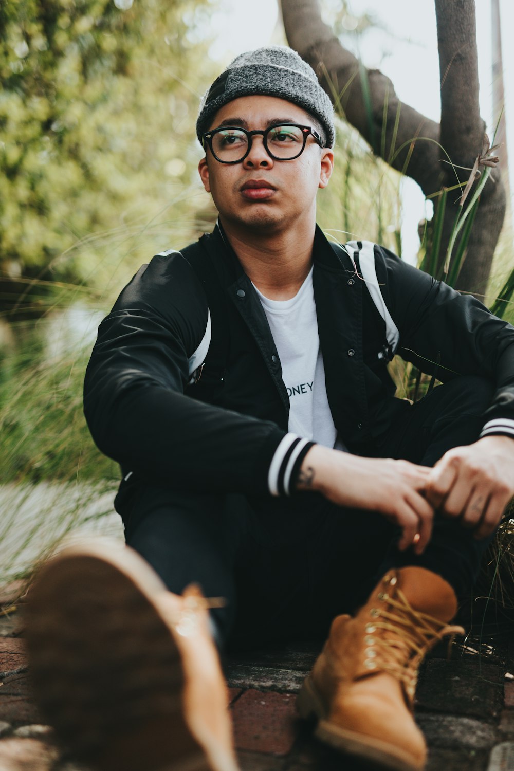 man wearing black jacket sitting near tree