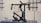 A professional camera stabilizer setup is displayed on a metallic surface against an industrial-style backdrop. The equipment consists of black components with multiple joints, handles, and electronic parts, indicating it is designed for filming and shooting stability.