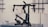 A professional camera stabilizer setup is displayed on a metallic surface against an industrial-style backdrop. The equipment consists of black components with multiple joints, handles, and electronic parts, indicating it is designed for filming and shooting stability.