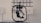 A black, mechanical device with a central structure enclosed in a circular frame is set against a gray industrial background. The device appears complex with multiple joints and components, possibly for engineering or robotics applications.