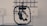 A black, mechanical device with a central structure enclosed in a circular frame is set against a gray industrial background. The device appears complex with multiple joints and components, possibly for engineering or robotics applications.