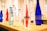 Several elegant glass and plastic bottles in various colors are arranged on a wooden table, creating an appealing display. The prominent bottle in the foreground is labeled with the word 'chic' and contains a red liquid, while others are either transparent or filled with water.