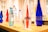 Several elegant glass and plastic bottles in various colors are arranged on a wooden table, creating an appealing display. The prominent bottle in the foreground is labeled with the word 'chic' and contains a red liquid, while others are either transparent or filled with water.