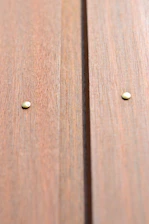 Close-up of rustic industrial nails piled on a wooden surface with yellow lighting.