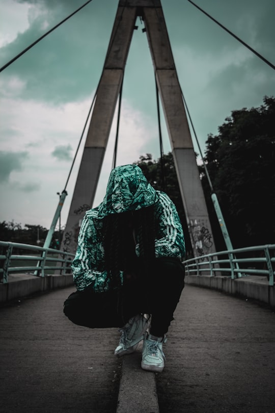 crouching person wearing track hoodie on bridge in Bogota Colombia