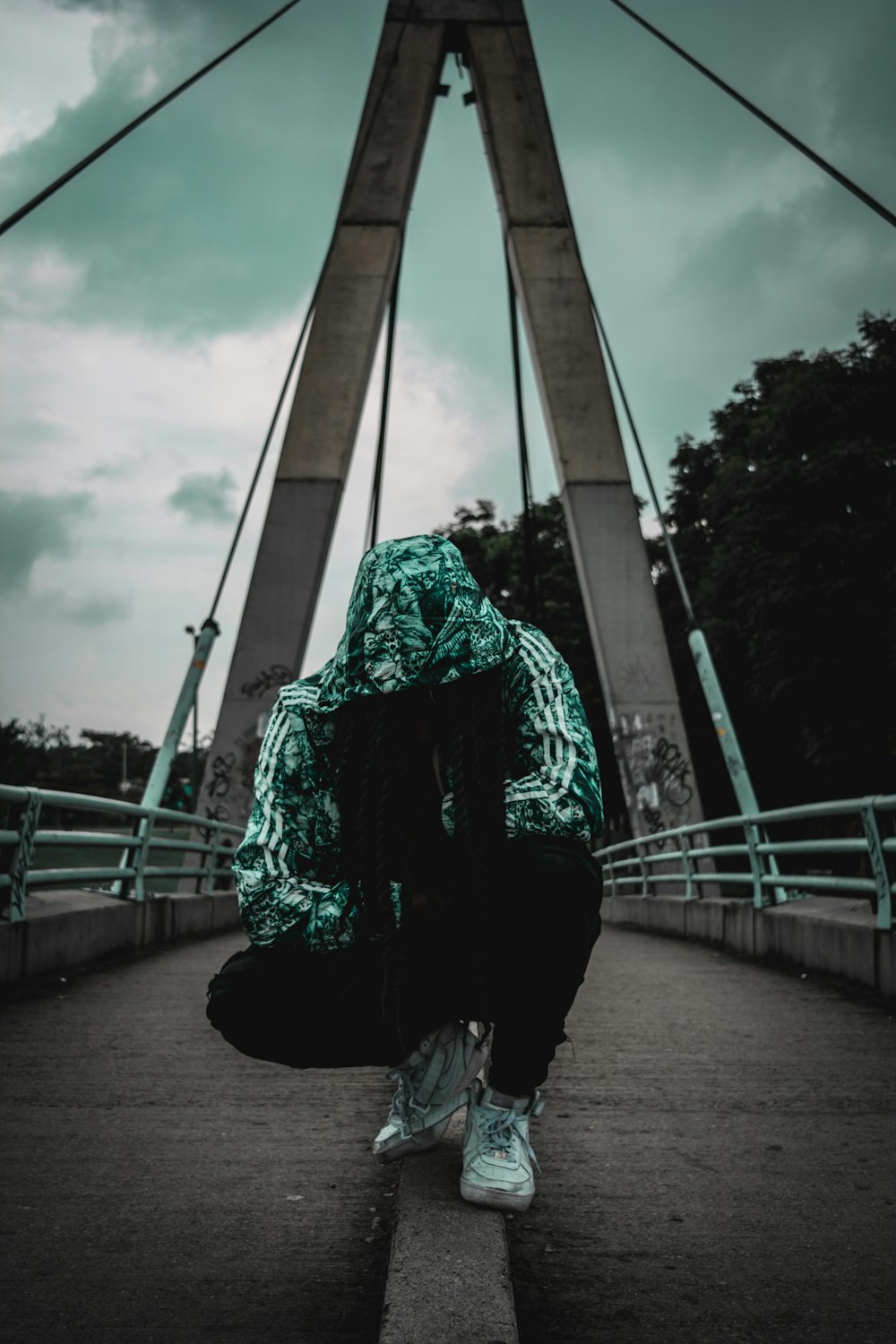 crouching person wearing track hoodie on bridge