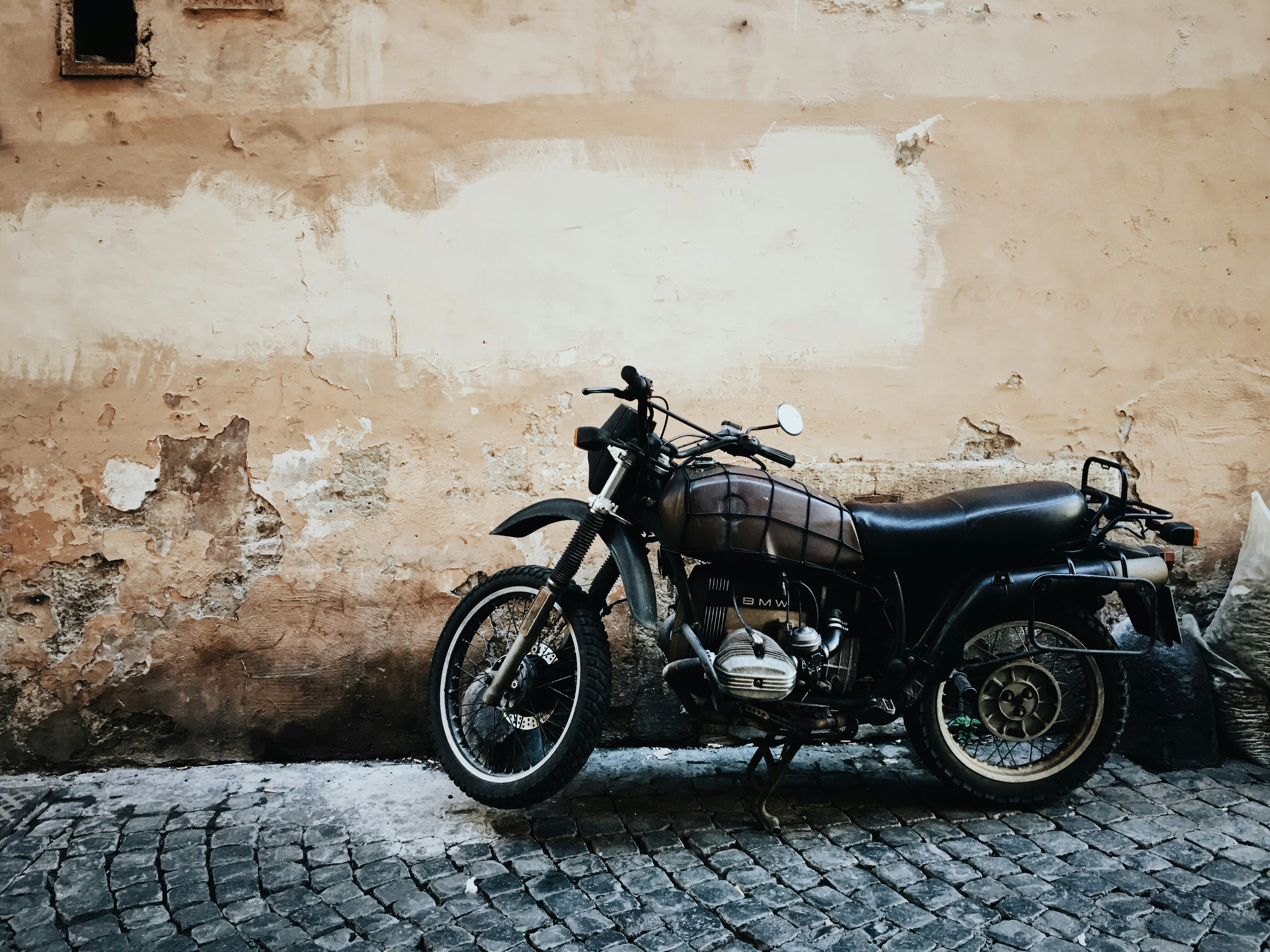 black and gray motorcycle parked on street beside wall at daytime