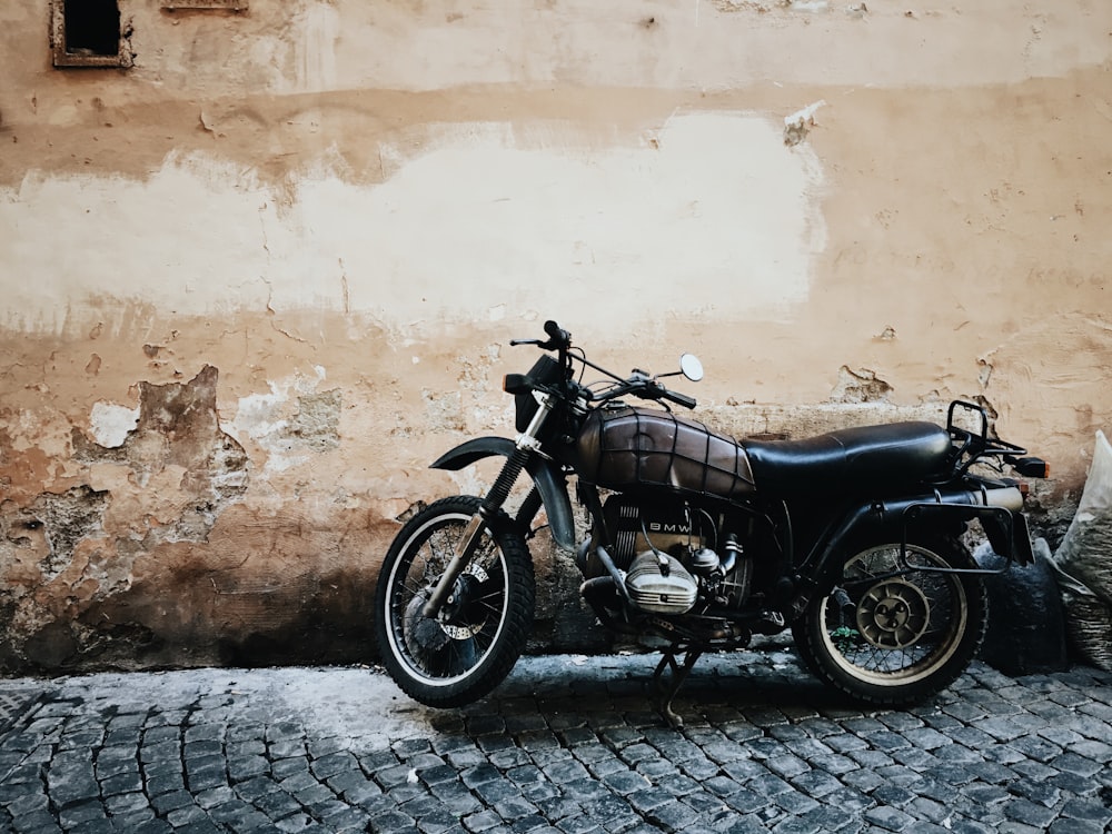 black and gray motorcycle parked on street beside wall at daytime