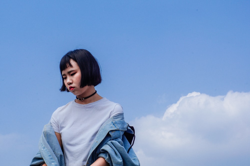 Femme portant une veste en jean bleue sous un ciel bleu nuageux