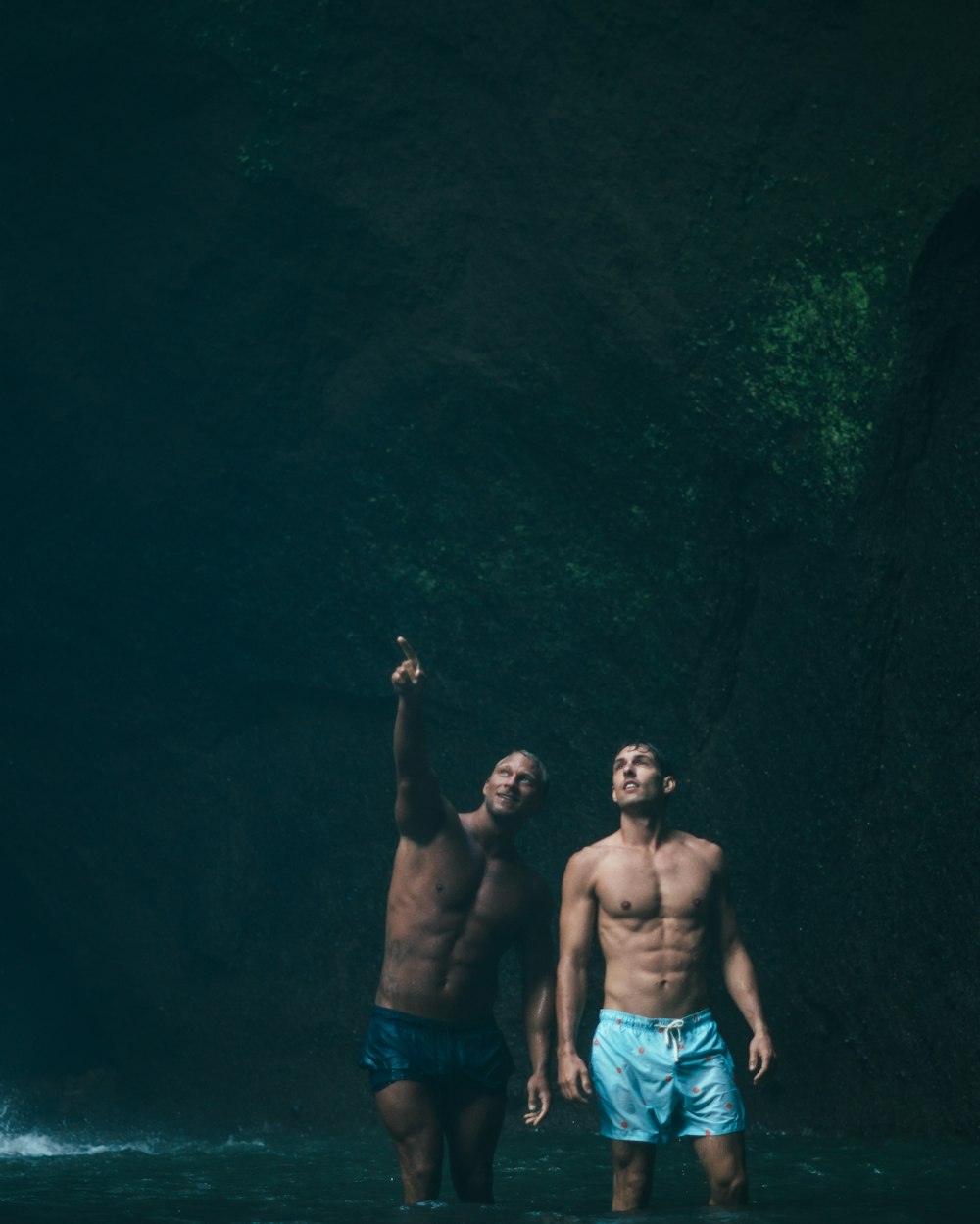 two men standing on body of water inside cave