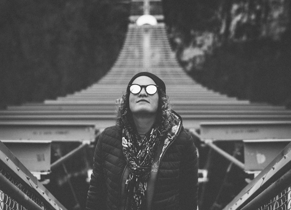 grayscale photography of woman standing while looking up on hanging bridge