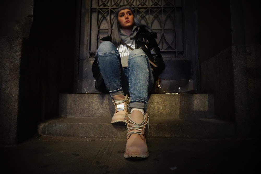 woman sitting on top of gray concrete stair near door