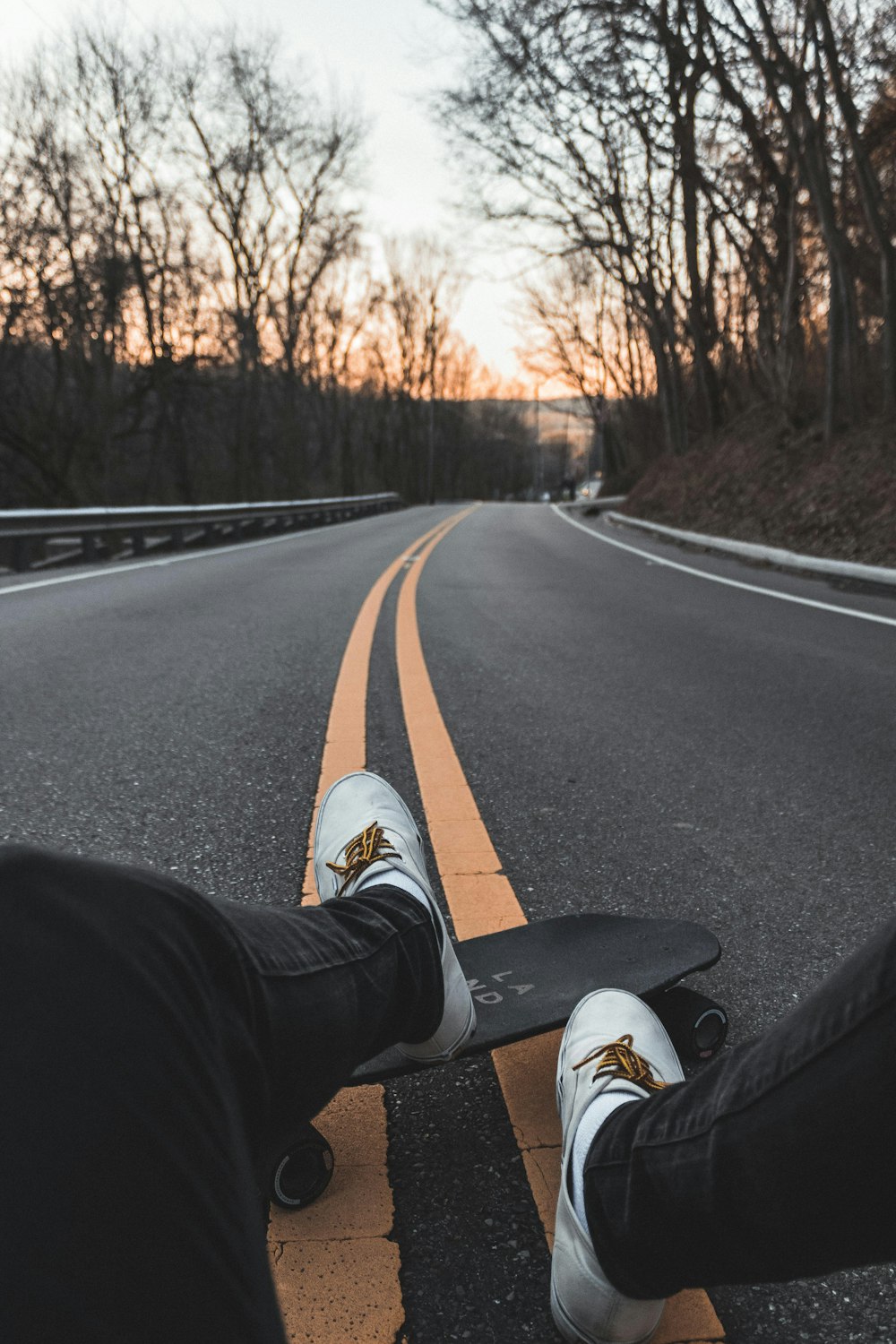 person wearing pair of white sneakers sitting on concrete road during daytime