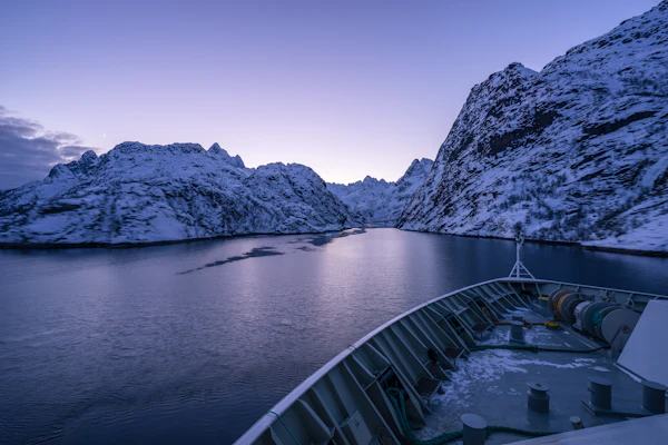 Ship on dark still water beneath snow-covered cliffs in Trollfjord, northern Norway
