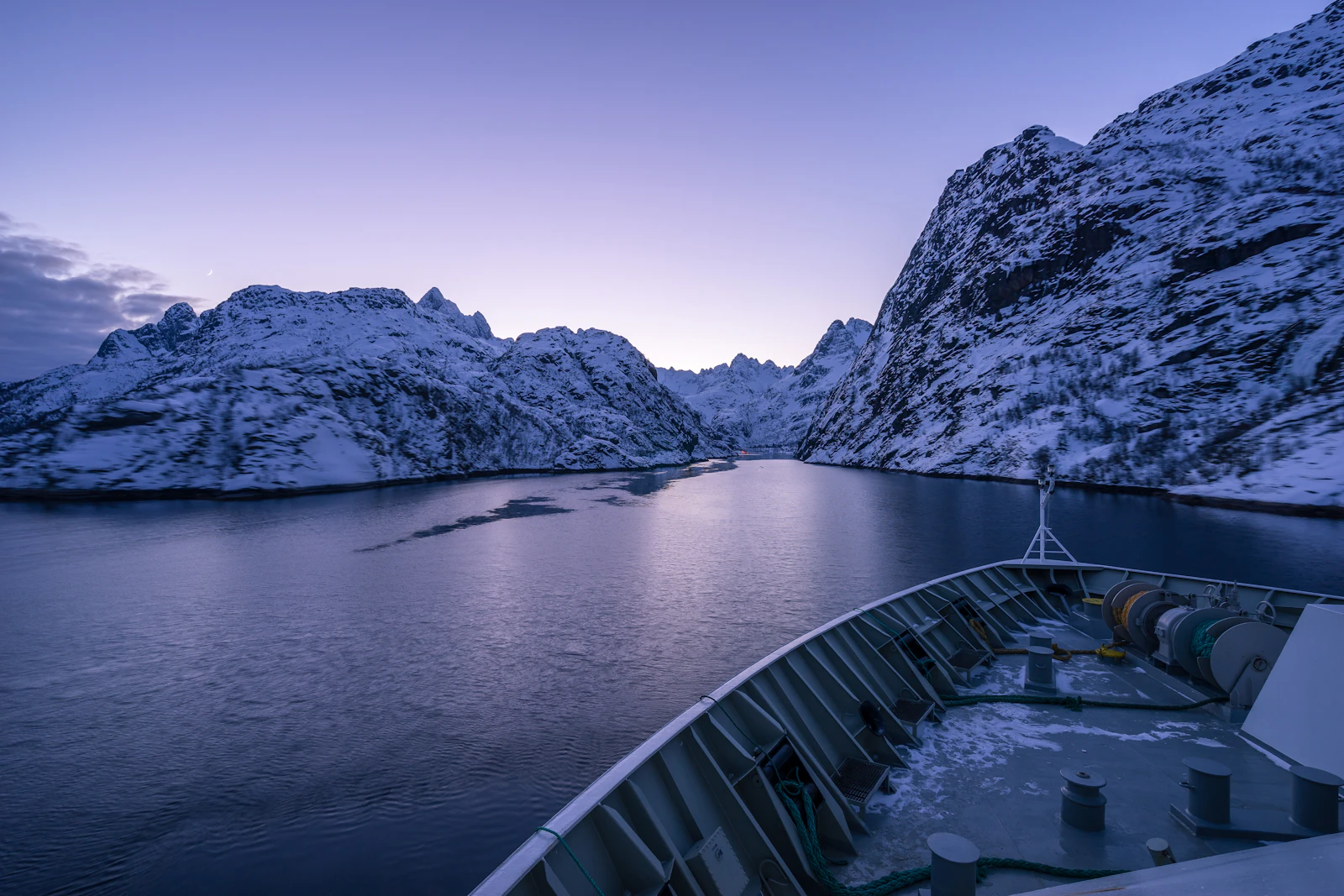 Ship on dark still water beneath snow-covered cliffs in Trollfjord, northern Norway