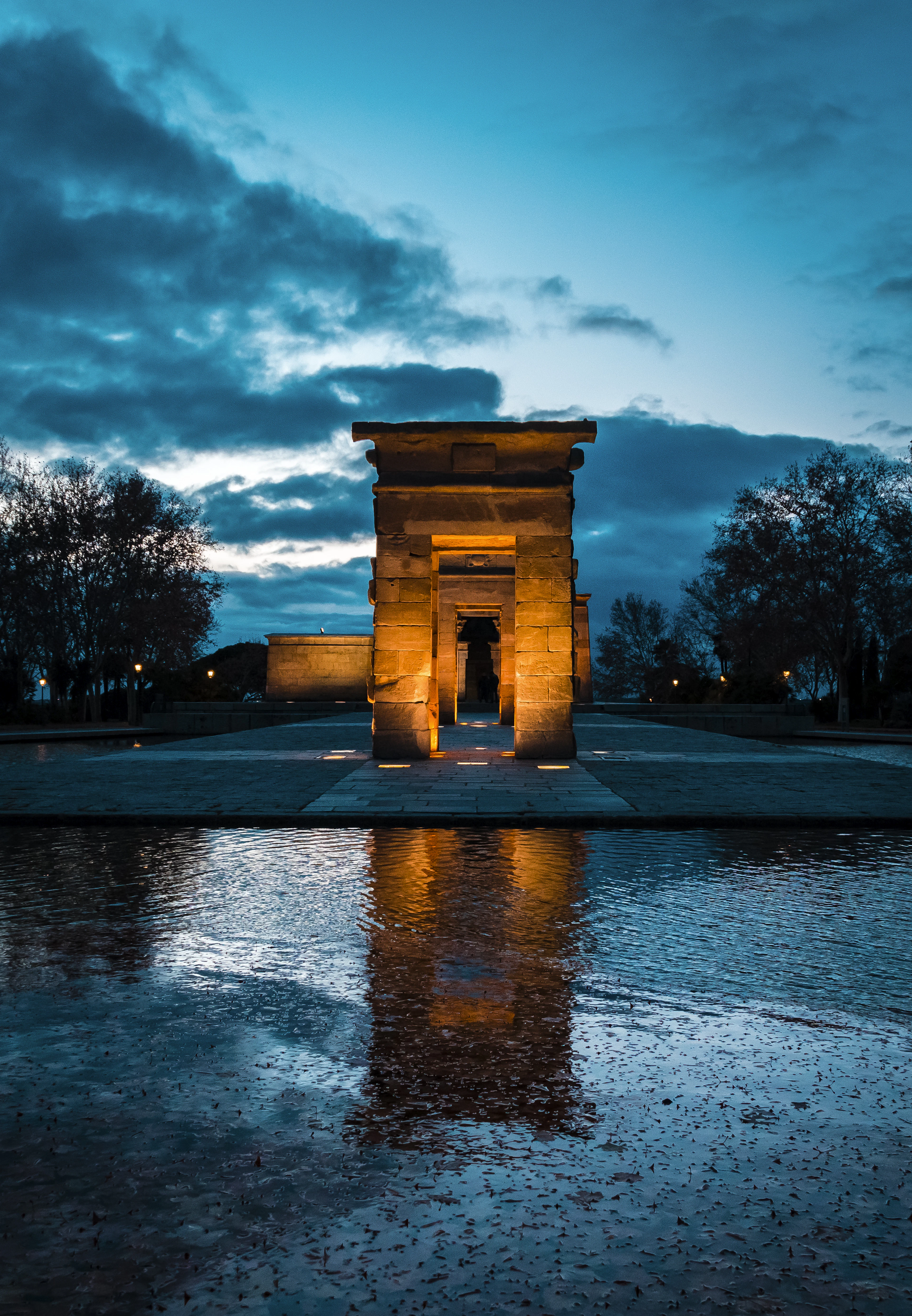The ancient Egyptian Templo de Debod floodlit at blue hour and mirrored in its reflecting pool in Madrid's Parque del Oeste