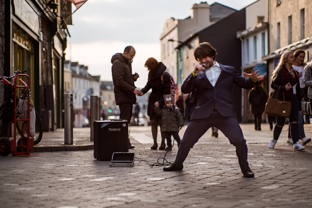 man singing outdoor using microphone and sound amplifier on road behind people