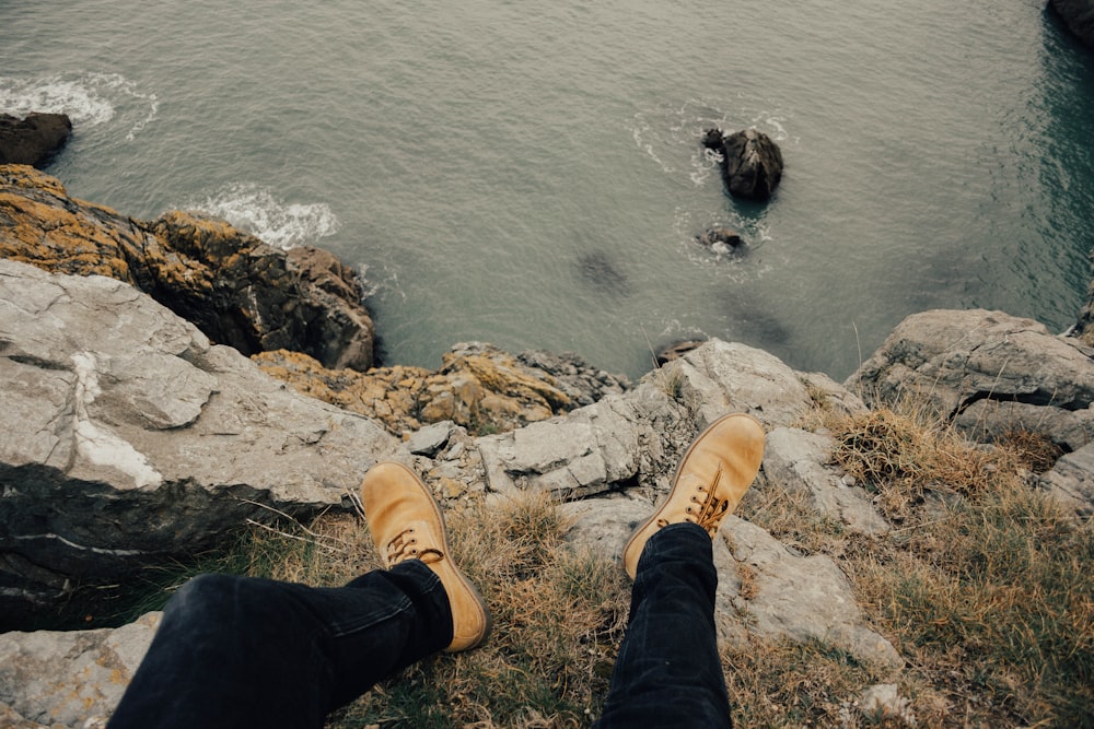 person wearing brown work boots sitting on cliff