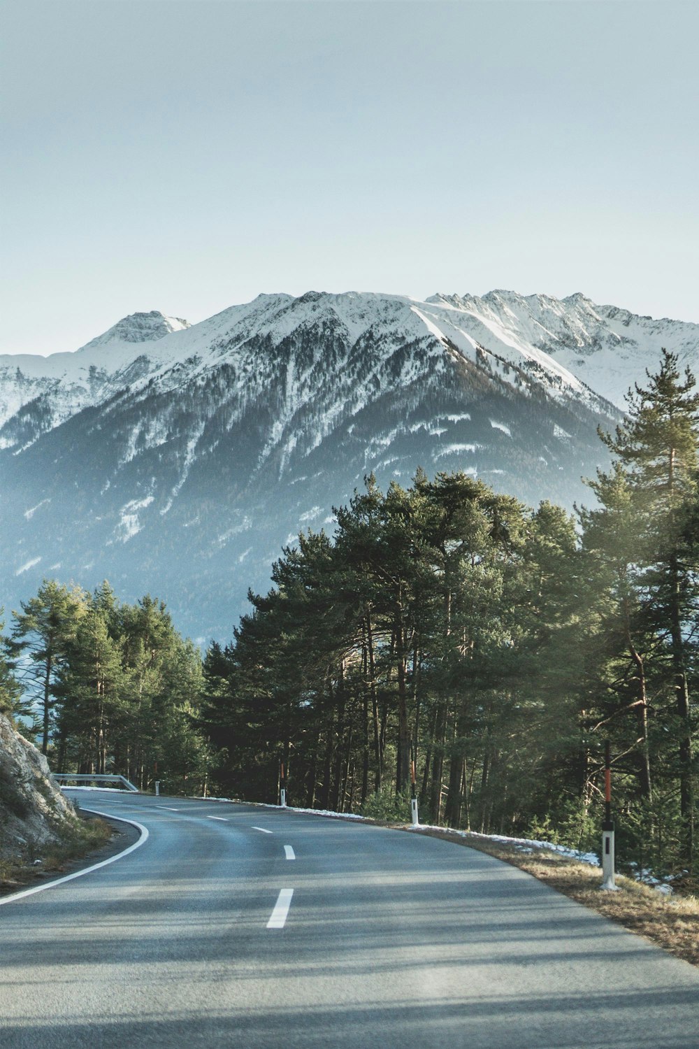 asphalt road beside of green trees in front of mountain covered of snow during daytime