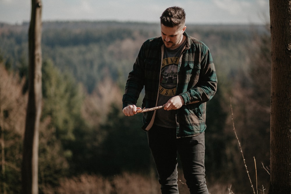 man in green and gray jacket holding brown stick near green leafed trees during daytime shallow focus photography