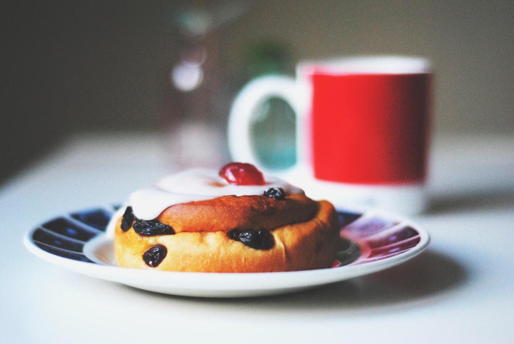 bread with raisins on saucer beside white and red mug