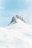 A snow-covered mountain peak rises prominently against a clear blue sky. The rugged rock formation of the peak contrasts with the smooth, gently sloping snow that covers the surrounding landscape.
