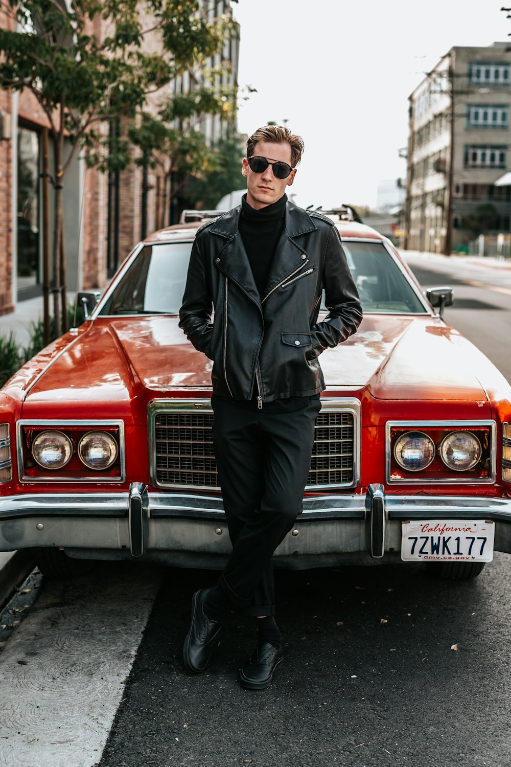 man leaning on red muscle car in street