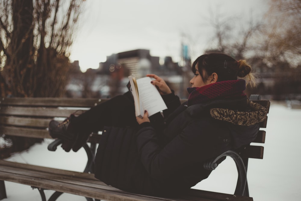 Femme inclinable sur un banc tout en lisant un livre au parc