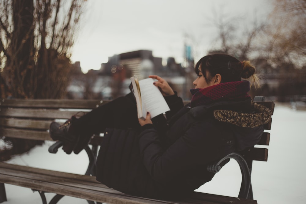 mulher reclinável no banco enquanto lê livro no parque