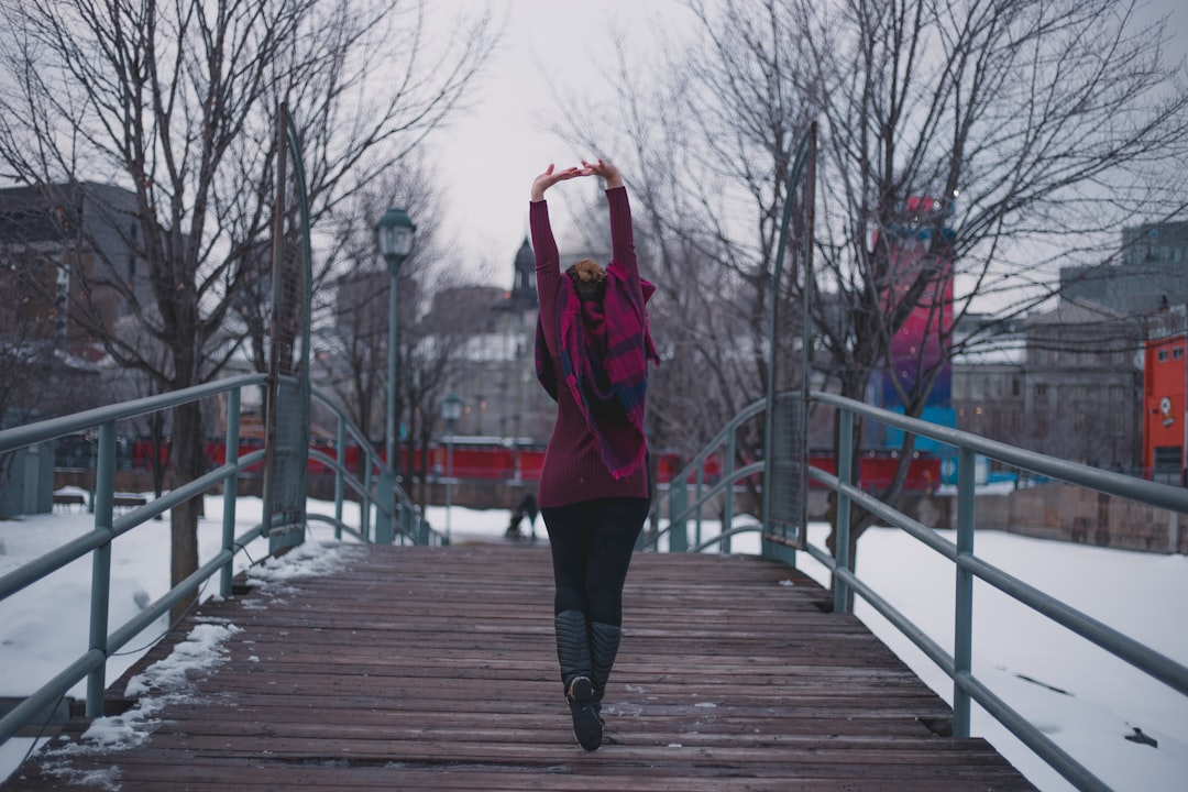 person wearing red jacket raising both hands while walking on brown wooden bridge during daytime