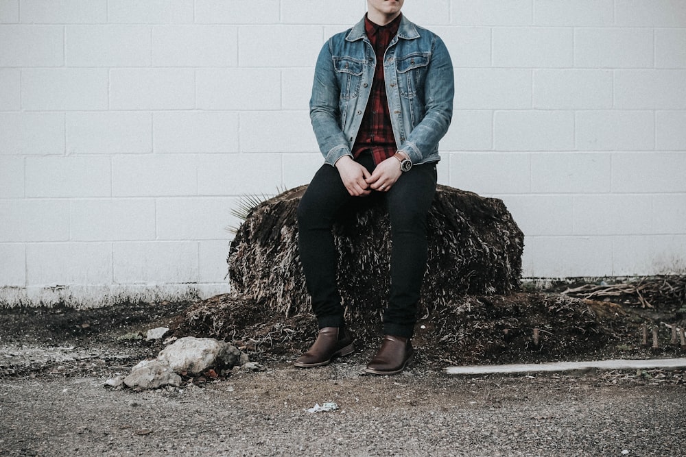 man wearing blue denim western shirt sitting next to white concrete wall