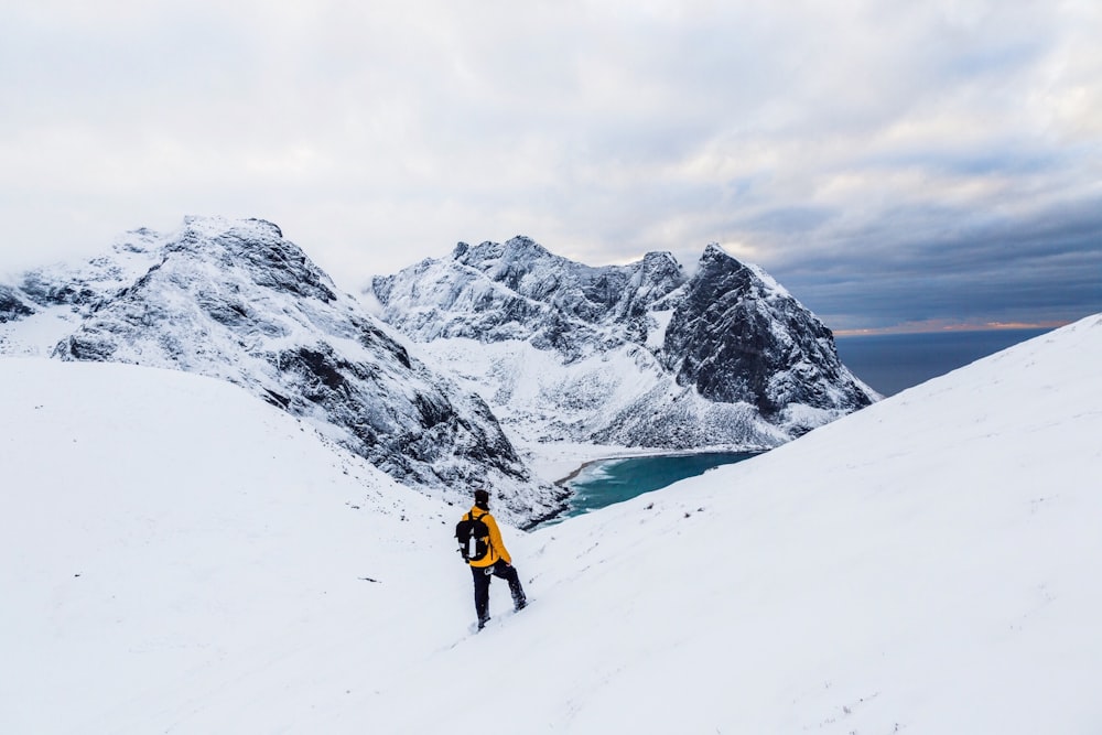 man wearing yellow jacket standing on white snowland at daytime