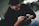 A focused man repairing a rifle with a laptop showing a detailed instructional video.