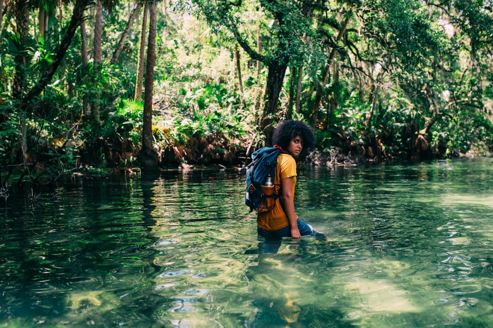 주황색 상의를 입은 사람이 배낭을 메고 낮에 숲에서 물 위를 걷고 있습니다.