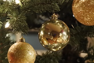 A close-up of shiny red and gold Christmas ornaments hanging on a beautifully lit tree.