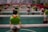 A close-up of a foosball table featuring a player figure wearing a green shirt and red shorts, mounted on a metal rod in the foreground with several similar figures in the background.