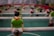 A close-up of a foosball table featuring a player figure wearing a green shirt and red shorts, mounted on a metal rod in the foreground with several similar figures in the background.