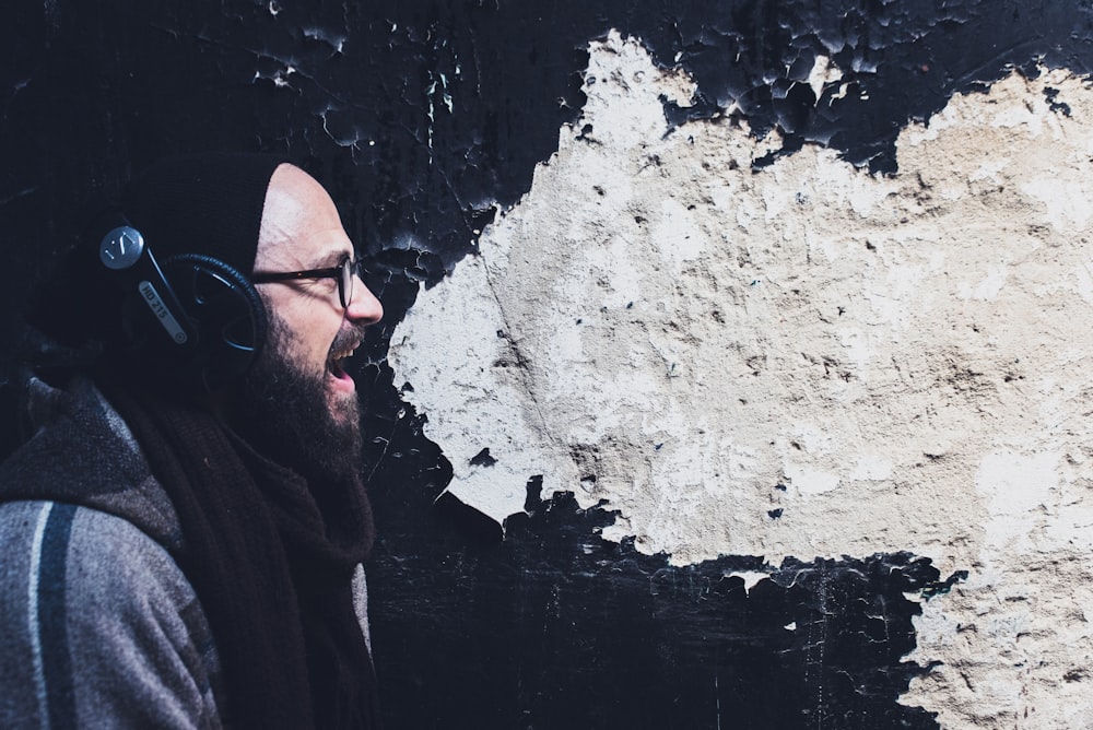 hombre usando auriculares gritando al lado de la pared