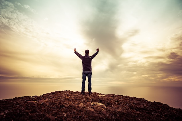A serene individual standing atop a mountain at sunrise, arms open wide embracing freedom and new beginnings.