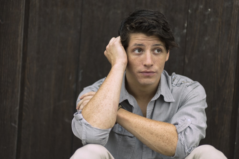 man wearing gray dress shirt leaning on brown wall