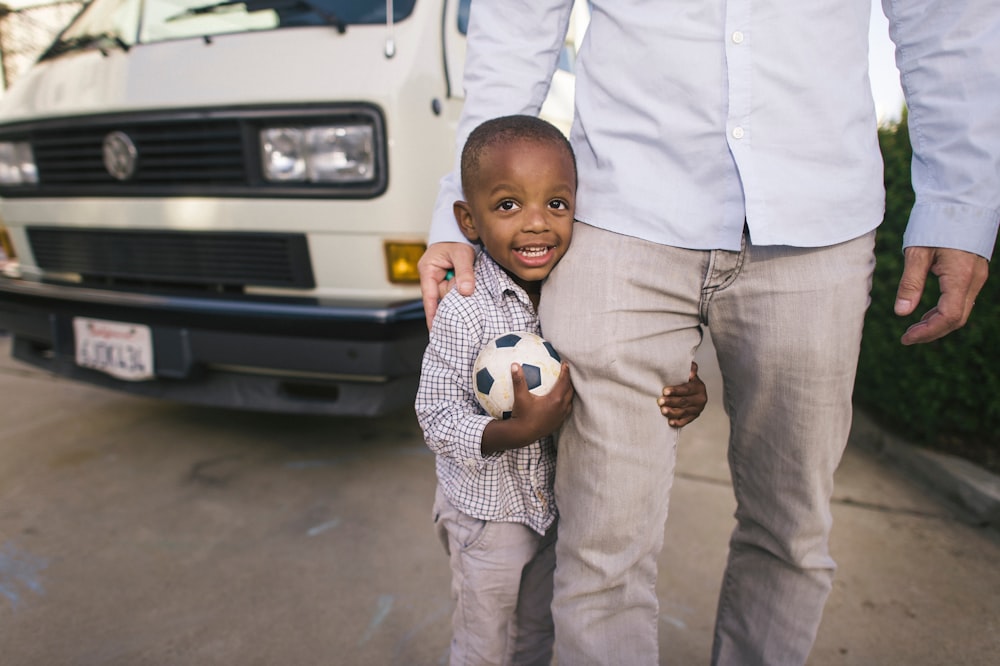 boy standing beside man in white dress shirr near vehicle