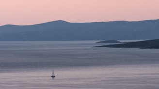 A serene Tunisian coastline at sunset with a sailboat gently gliding on calm waters.