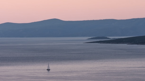 A serene Tunisian coastline at sunset with a sailboat gently gliding on calm waters.
