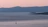 A serene Mediterranean coastline at sunset with a small sailboat gliding quietly on calm waters.