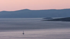 Silhouette of a lone sailboat drifting on a peaceful ocean horizon at dusk.