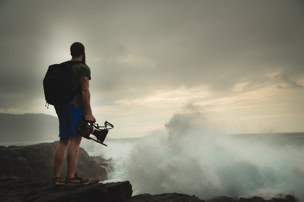 man standing on rock cliff near body of water