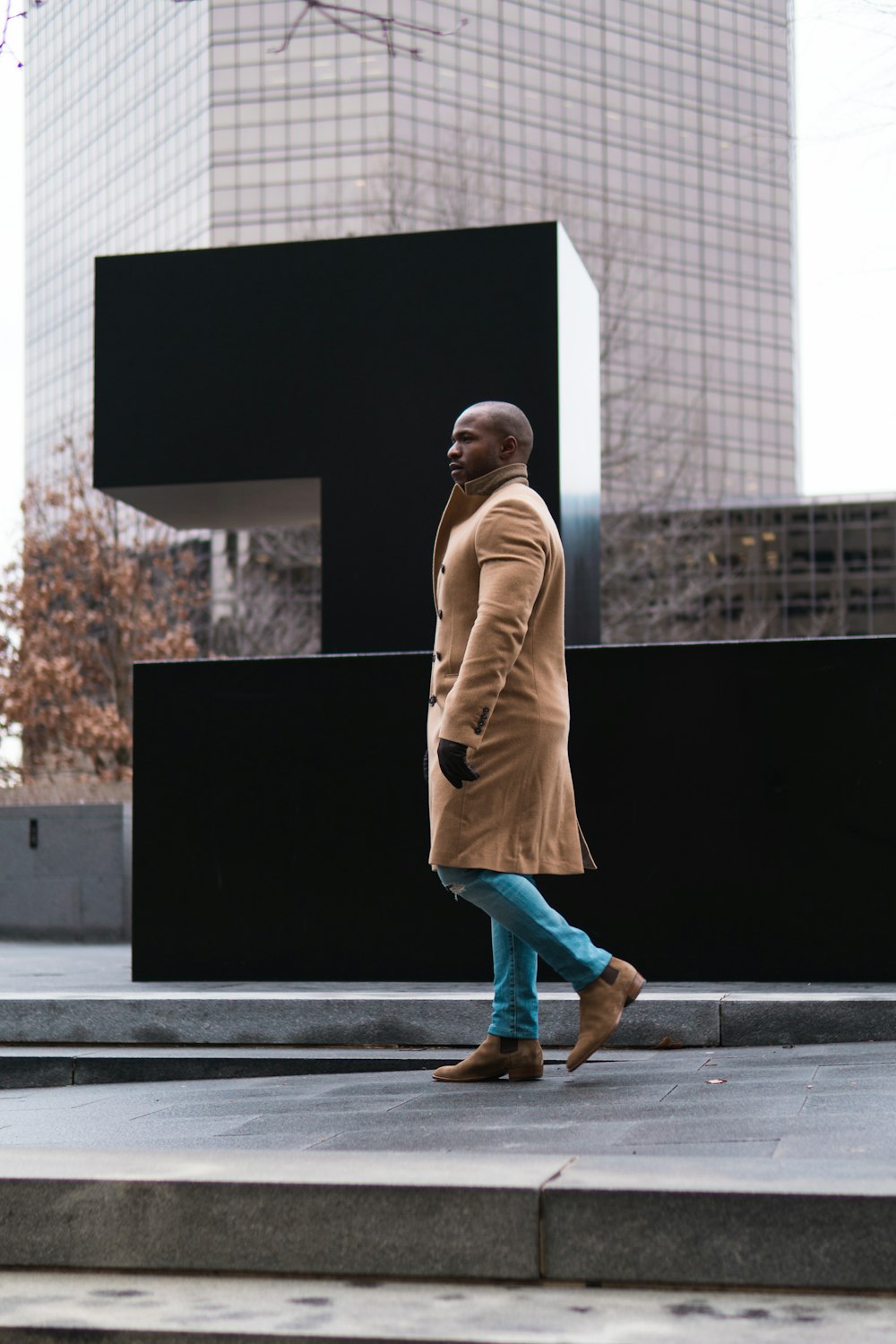 uomo che indossa un cappotto marrone che cammina vicino al monumento nero durante il giorno